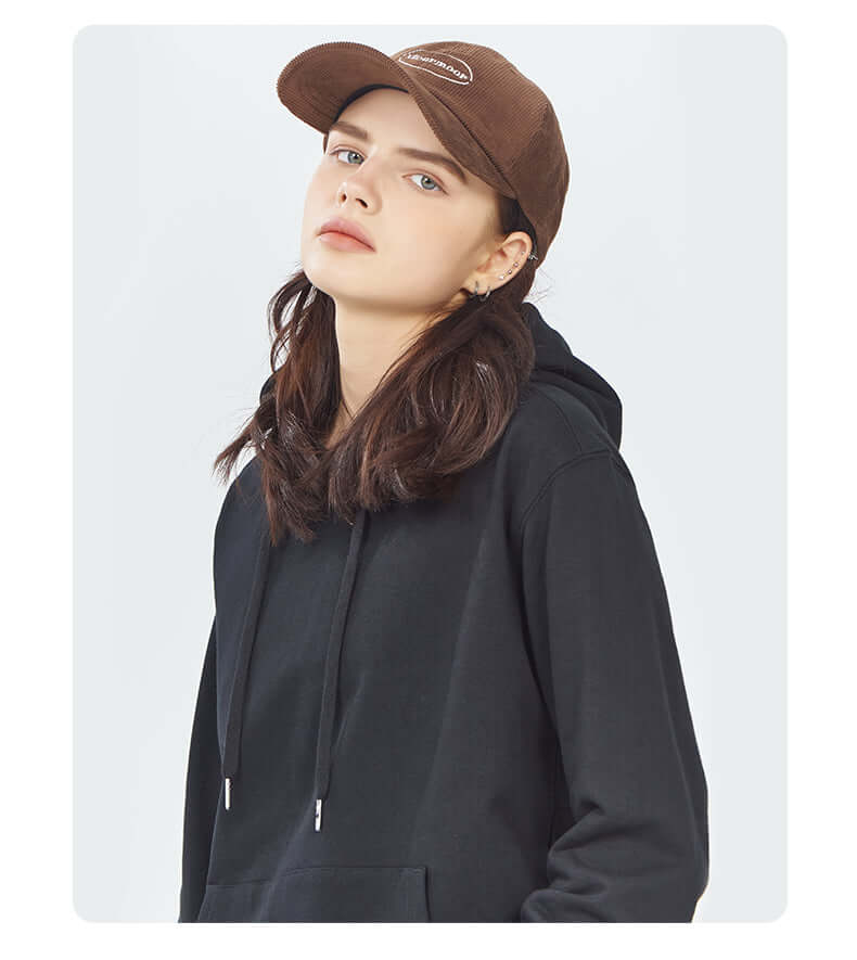 Model wearing a black blank hoodie wholesale with a brown cap, showcasing a stylish and casual look.