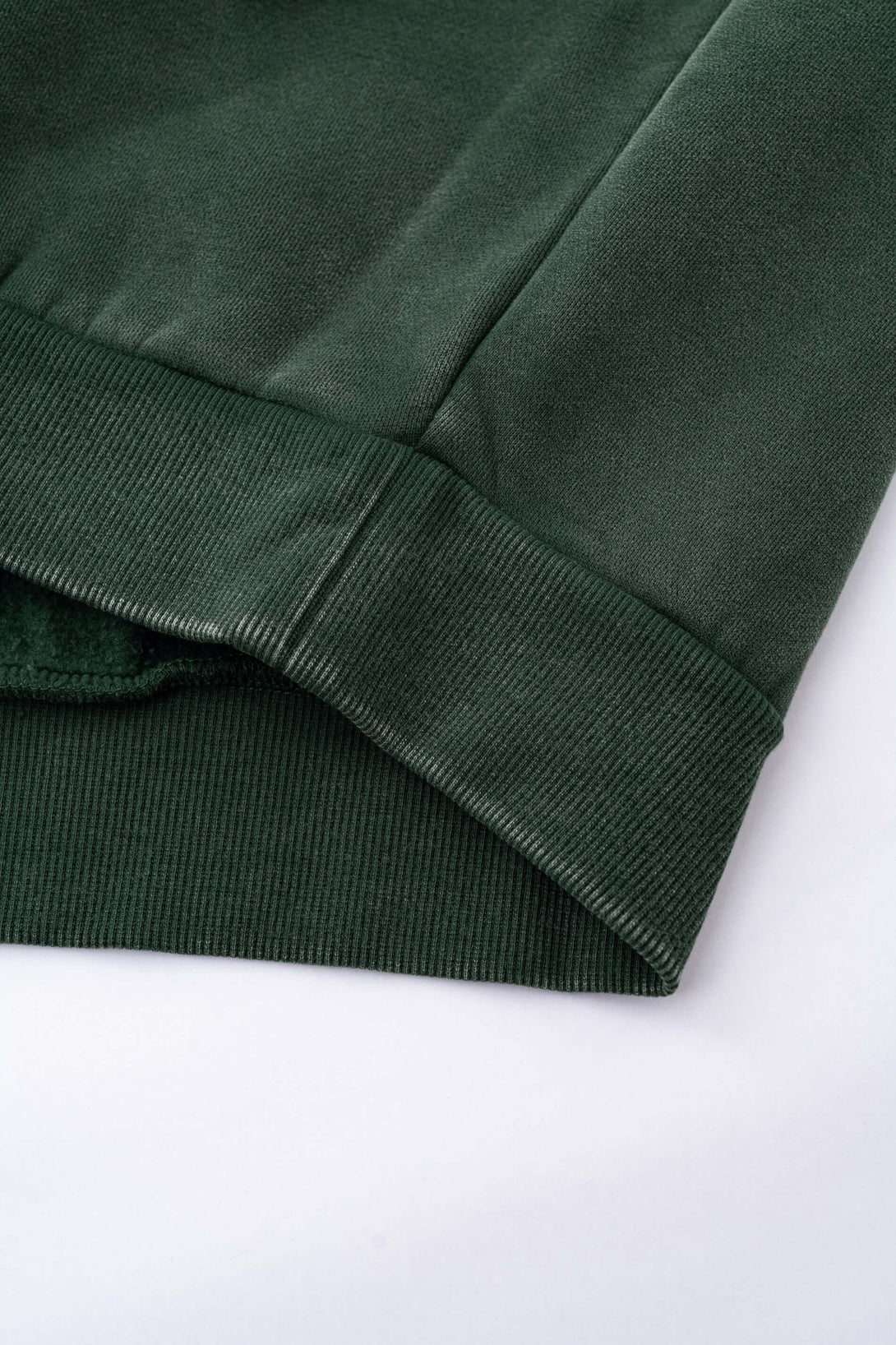 Close-up of the cuff and hem of the Distressed Panel Crewneck, showcasing the rich green fleece-lined fabric.