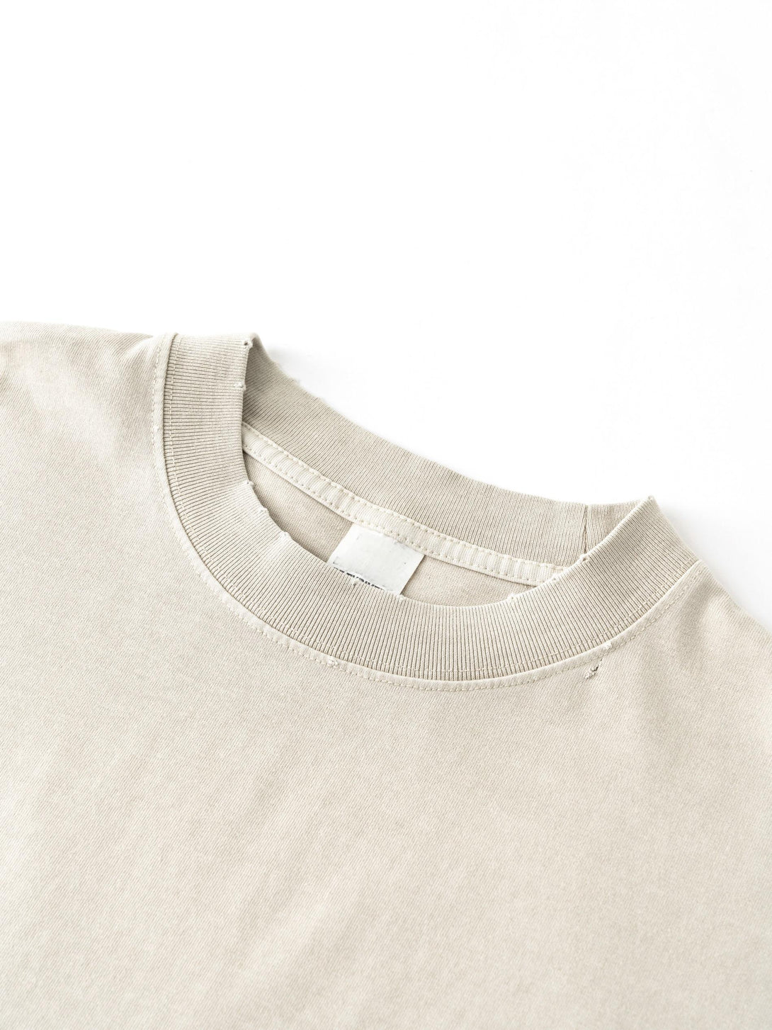 Raw-edge collar construction on Apricot oversized tee, garment manufacturing technique close-up.
