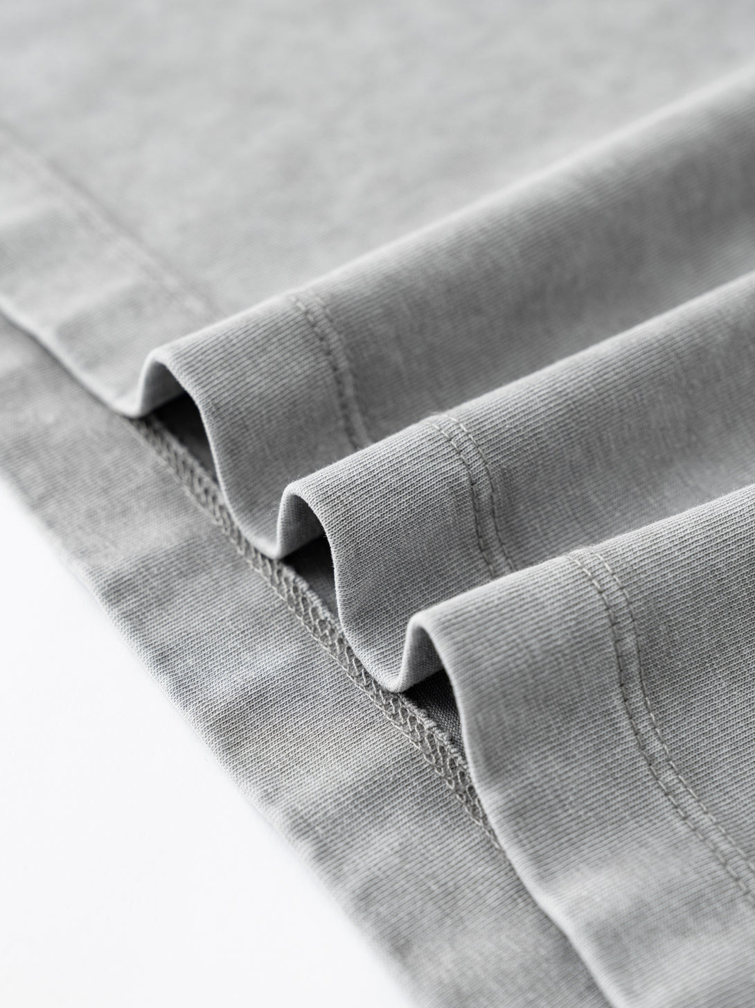 Distressed hem texture with vintage wash effect on Unisex Light Gray oversized cotton tee.