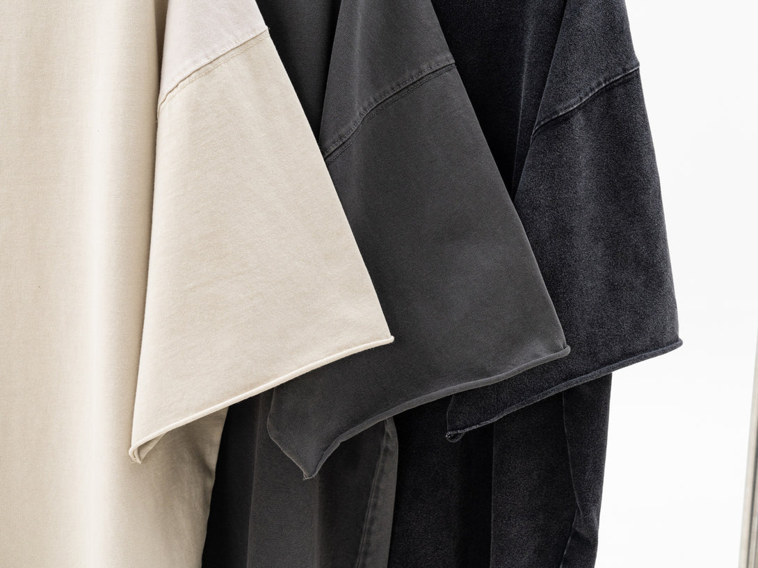 Hanger display of Pigment Dye Oversized Tees in Apricot, Dark Gray and Black colors, showing garment drape for wholesale bulk orders. 